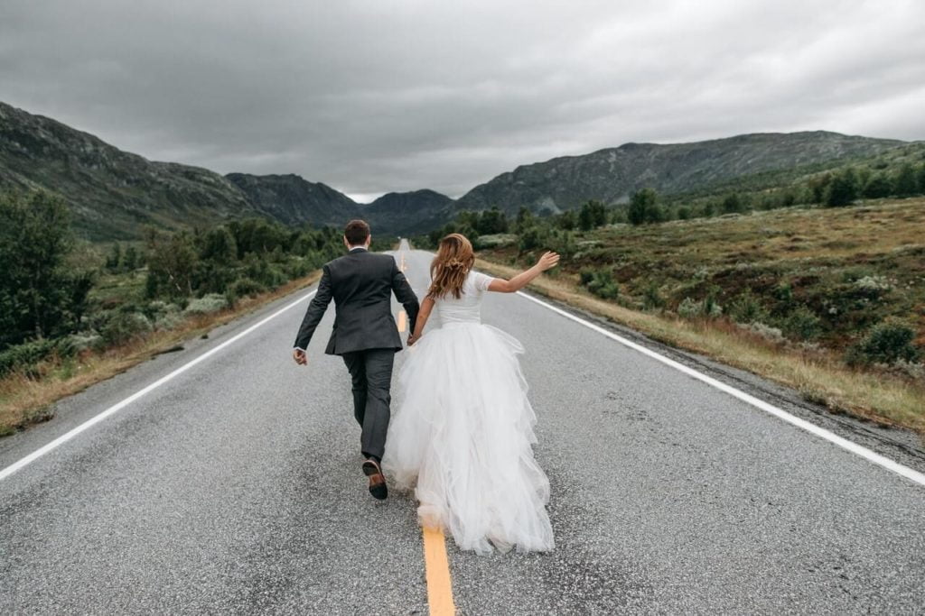 a man and woman walking down a road with mountains in the background
