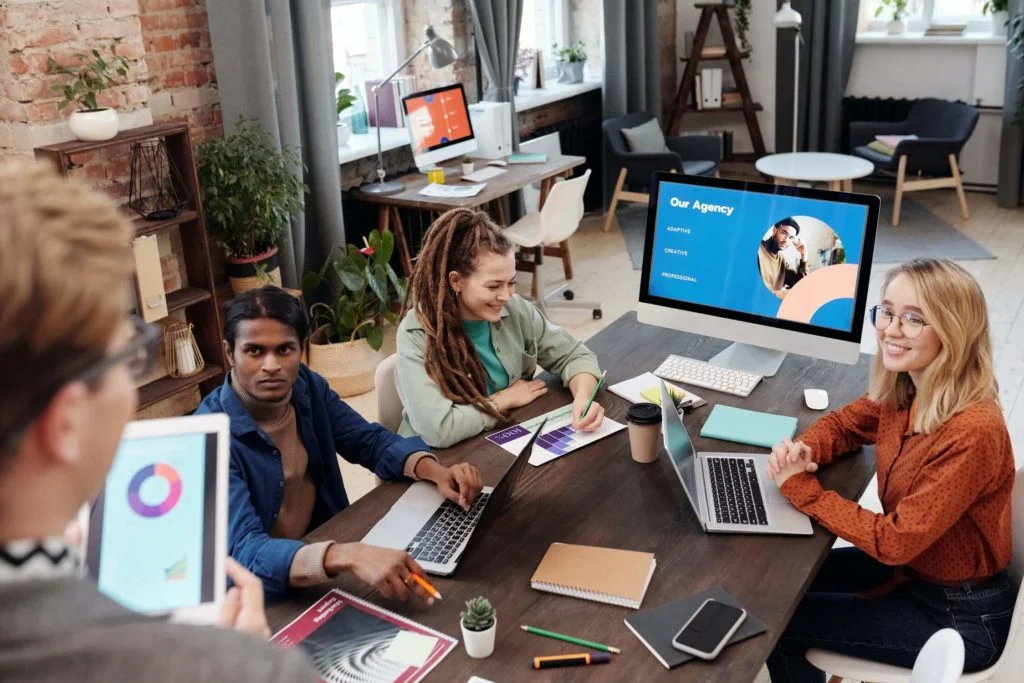 a group of people sitting around a table with laptops